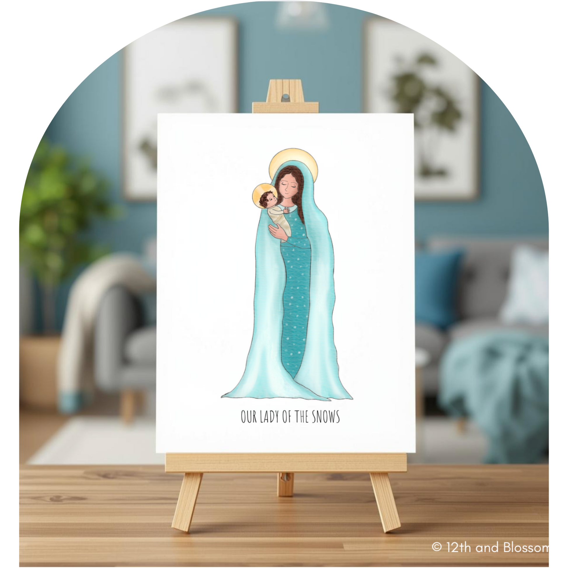 A vertical art print on a white canvas, displayed on a small wooden easel. The print features an illustration of Our Lady of Snows in a light blue gown holding baby Jesus, with the text 'OUR LADY OF THE SNOWS' below.
