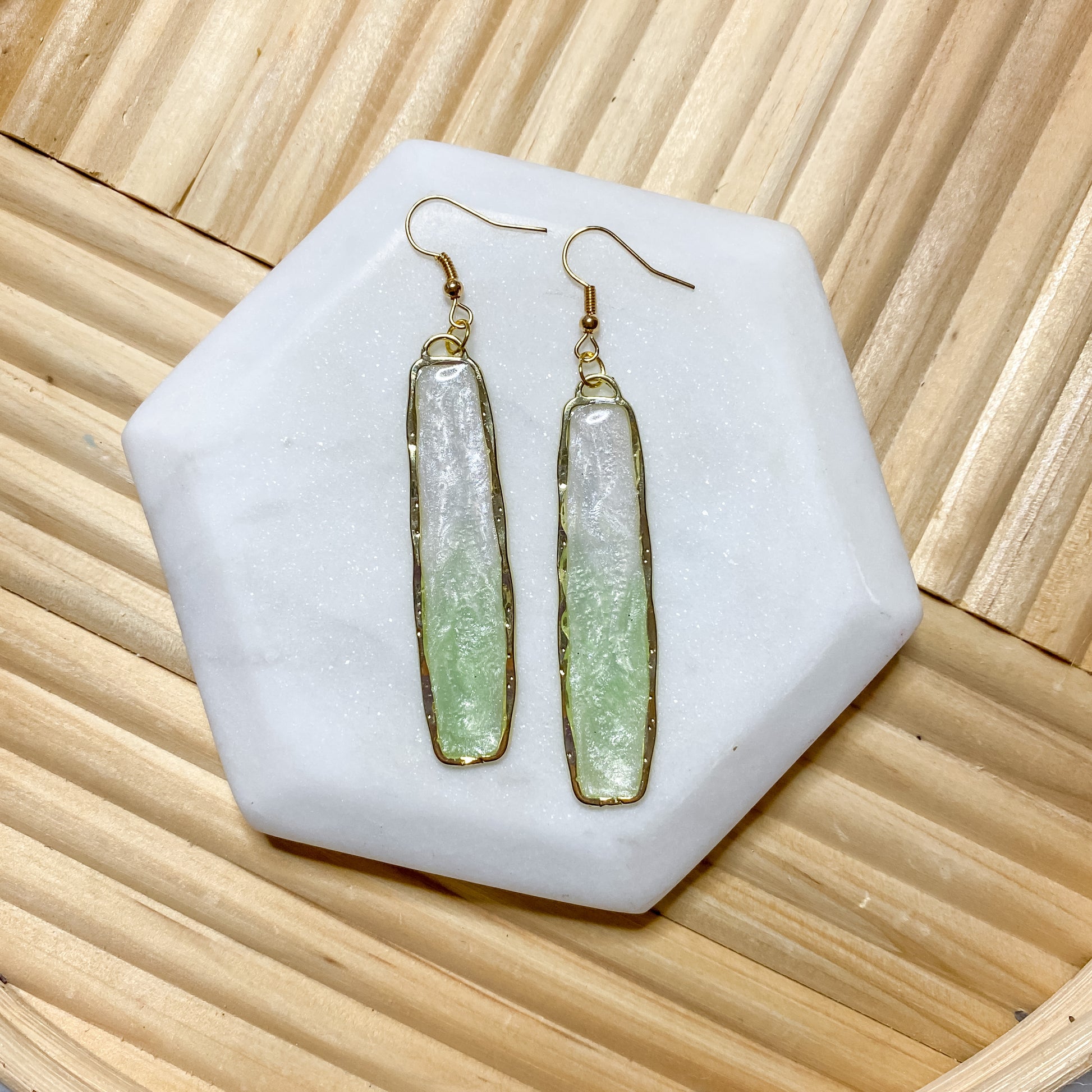 A pair of handcrafted earrings featuring white and light green resin, gold plated alloy bezel oval ring, displayed on a flat surface.